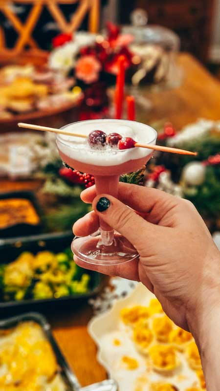 Holiday bourbon cocktail topped with egg foam and sugared cranberries in a coup glass